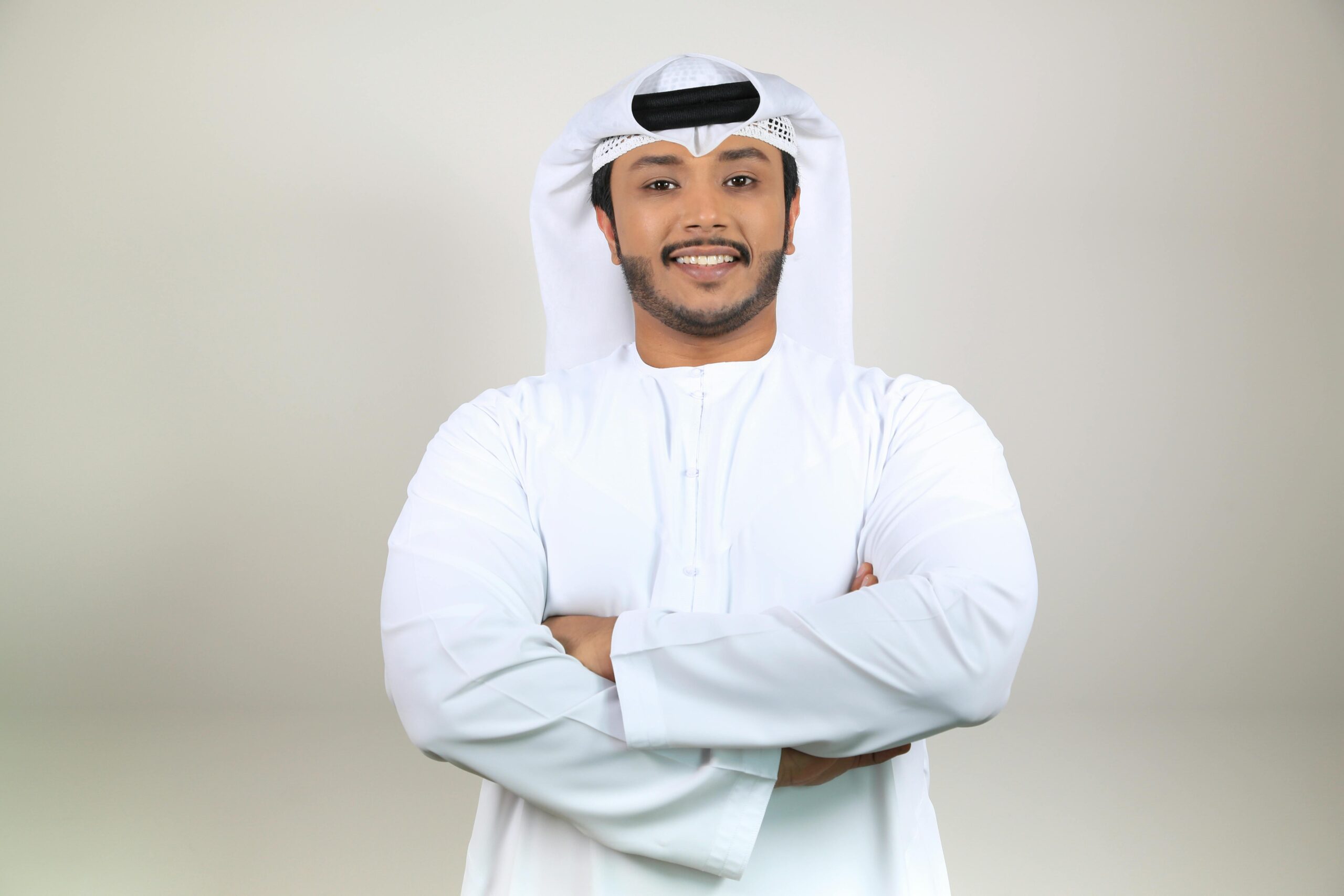 Home Confident Middle Eastern man smiling in traditional attire with crossed arms, studio portrait.